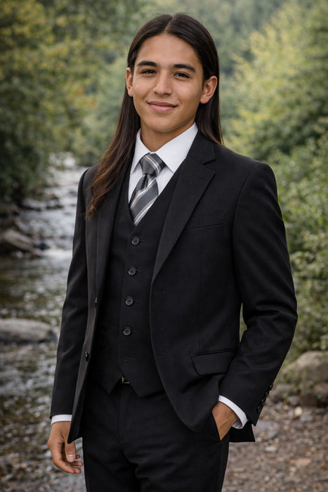 Young man in matte black formal suit and tie standing by a riverside outdoors