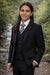 Young man in matte black formal suit and tie standing by a riverside outdoors