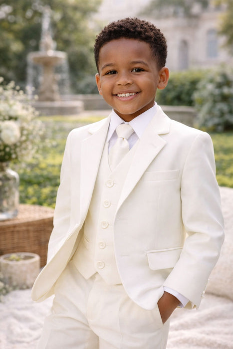 8041 Ivory pre-teen suit shown on a smiling boy outdoors with greenery and a fountain in the background.