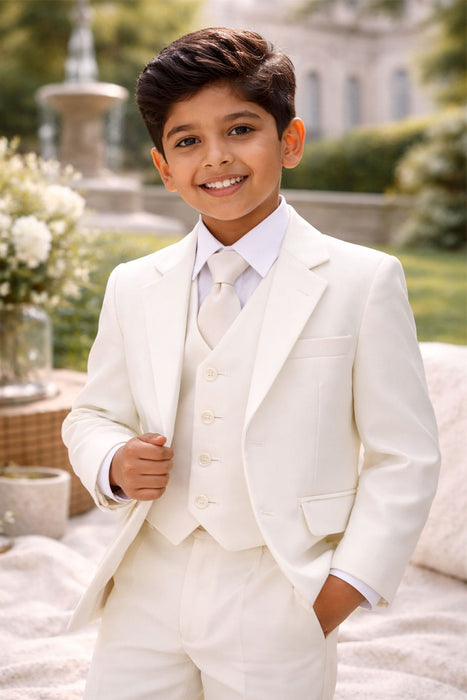 Young boy in an ivory three-piece suit smiling outdoors, perfect for formal events or special occasions.