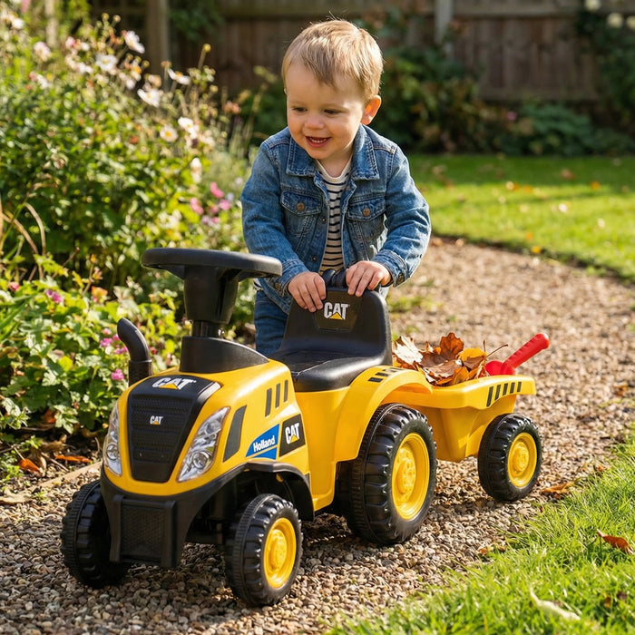 CAT ride-on toy truck with child pushing it outdoors on a garden path, leaves in the wagon.