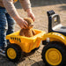 CAT ride-on toy truck outdoors with child placing a teddy bear in the yellow dump bed.