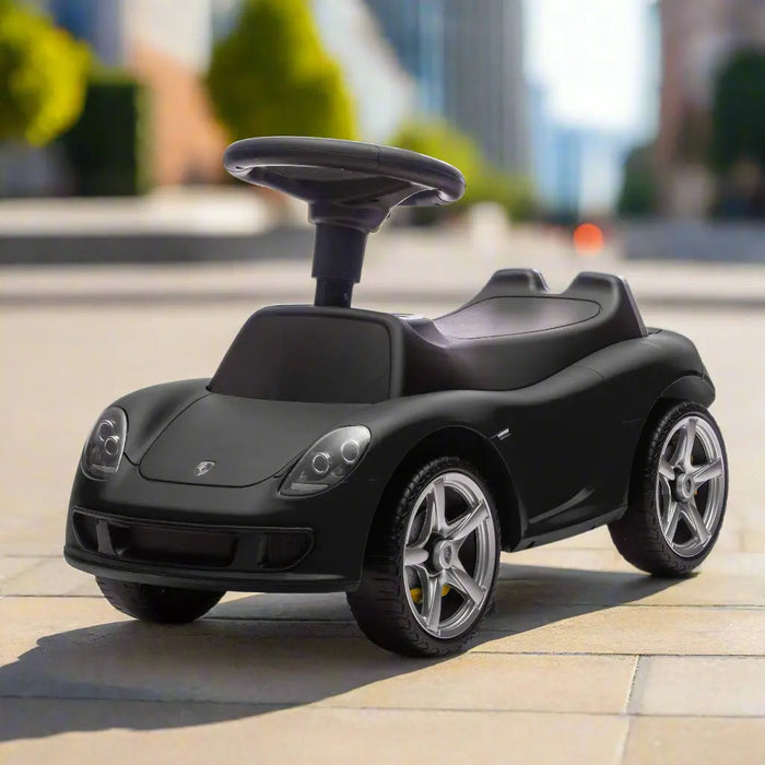 Black ride-on toy car for kids shown outdoors on a city sidewalk in daylight.