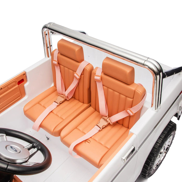 Kids ride-on car tan seats with seat belts, shown from above inside a white toy vehicle.