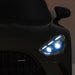 Kids electric ride-on car close-up showing bright LED headlights in a dark indoor setting.