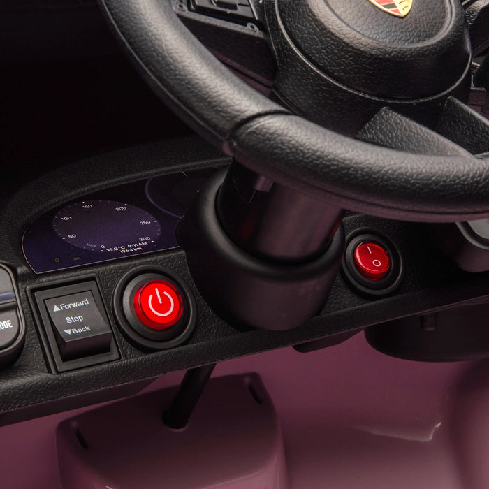 Pink ride-on toy car dashboard closeup showing steering wheel, power button, and control panel.