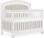 White wooden baby crib with tufted beige upholstered headboard and soft bedding