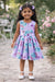Roses Butterflies Silky Dress in lilac worn by a young girl outdoors with garden flowers.