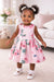 Roses & Butterflies Silky Dress shown on a smiling toddler girl standing in a cozy living room.