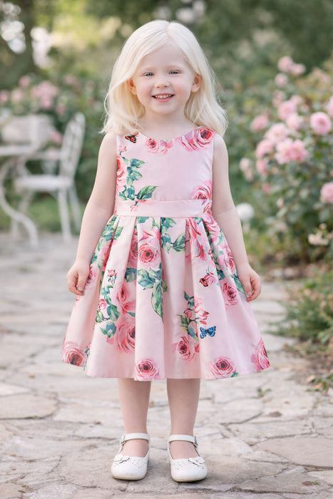 Girl wearing pink roses and butterflies silky dress standing outdoors on a garden path