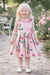 Girl wearing pink roses and butterflies silky dress standing outdoors on a garden path