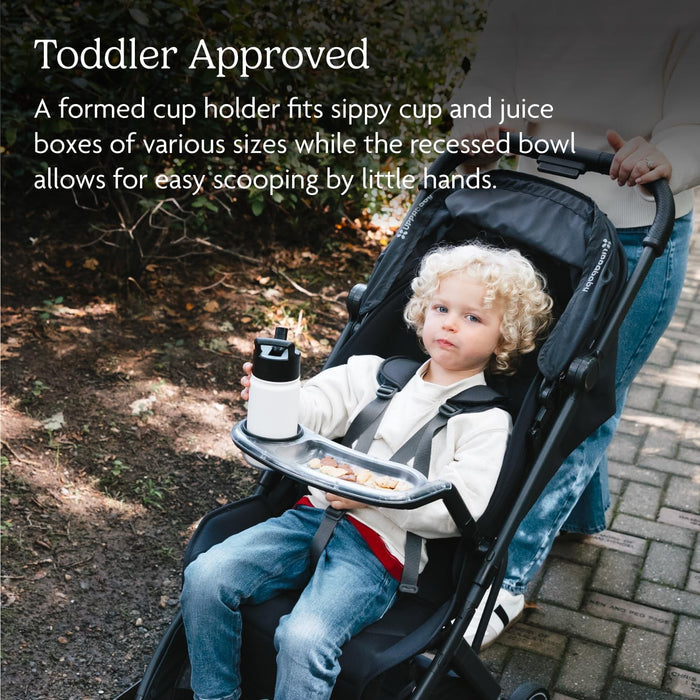 Toddler in stroller holding sippy cup with snack tray, outdoors on walking path