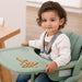 Smiling toddler in high chair with safety harness, eating snacks from tray indoors
