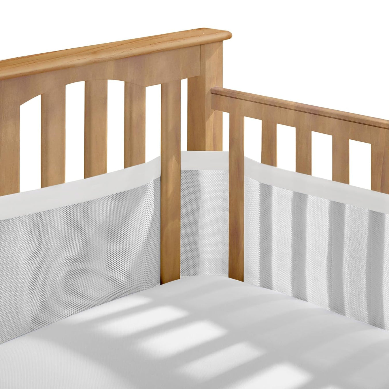 Wooden baby crib with white breathable mesh crib liner in nursery setting