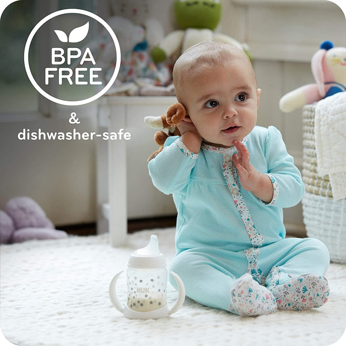 NUK baby sippy cup placed on a soft rug in front of a baby in a cozy nursery setting.