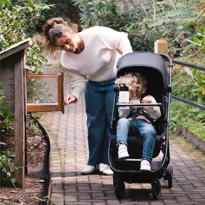 Woman with a toddler in a black stroller on a garden path, outdoor baby stroller walk