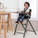 Toddler sitting in a modern high chair with safety harness in a bright kitchen