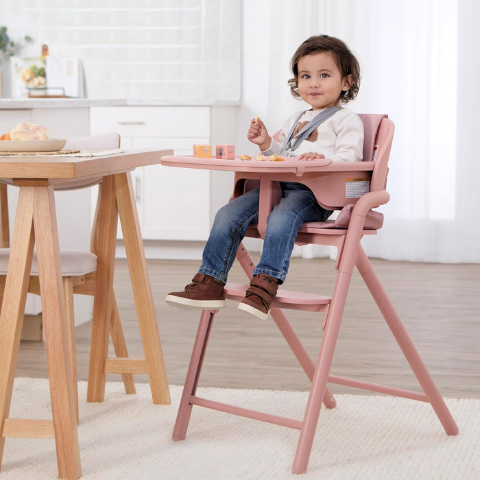 Smiling toddler sitting in a pink high chair at a dining table in a bright kitchen