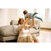 Mother holding smiling baby in blue outfit while playing on living room floor by a grey sofa.