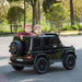 Kids electric ride-on SUV car outdoors with two children sitting inside, black model on paved road.