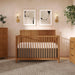 Modern wooden baby crib in nursery with mattress, wall art and plants