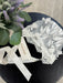 Teter Warm AB06 bonnet with 3D leaves and lace trim displayed on a black table beside flowers.