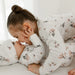 Two young children in matching white floral bamboo pajamas cuddle on a bed.