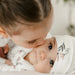 Older child kissing baby in floral bamboo sleeper and hat, cozy sibling moment