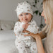 Baby wearing white bamboo sleeper pajamas and hat with squirrel print, held by smiling woman