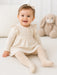 Bellissima ecru white baby tights shown on a smiling baby sitting on a soft white blanket indoors.