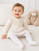 Bellissima ecru white baby tights worn by a smiling baby sitting on a soft cream blanket.