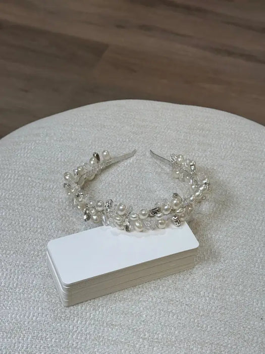 Pearl and silver decorative headband displayed on a textured light surface beside blank cards.