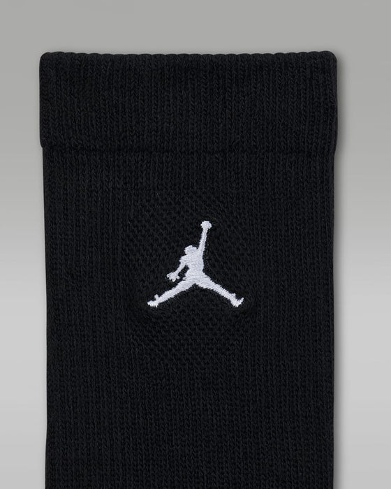 Black children’s crew sock with white embroidered logo on the cuff, shown against a gray background.