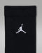 Black children’s crew sock with white embroidered logo on the cuff, shown against a gray background.