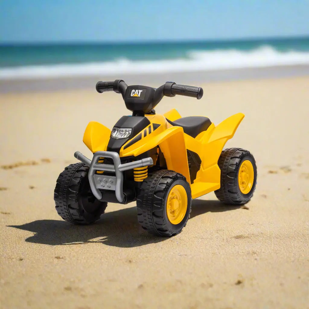 CAT yellow and black toy quad bike with large wheels shown on a sandy beach.