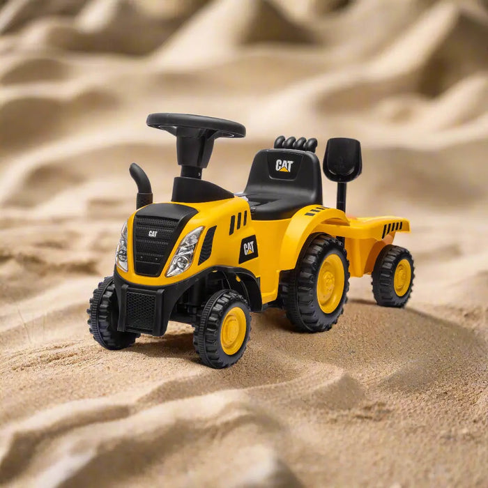 CAT yellow ride-on toy tractor with trailer displayed on sandy terrain.