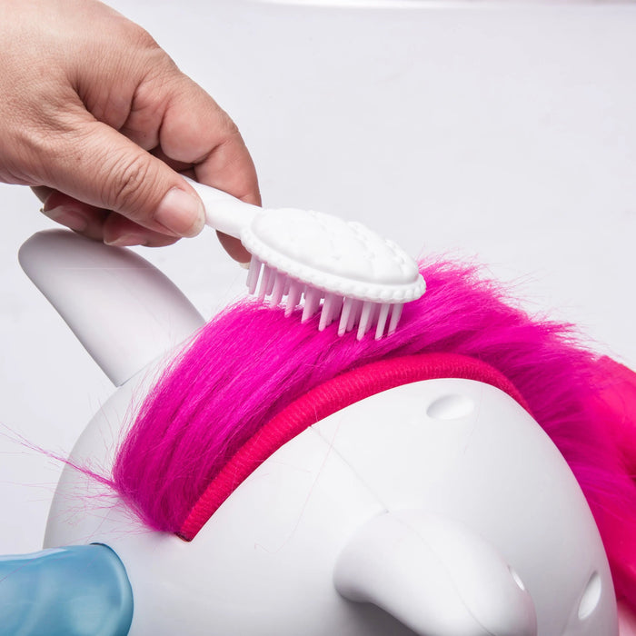 Unicorn toy with pink mane being brushed by a hand using a white brush
