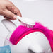 Unicorn toy with pink mane being brushed by a hand using a white brush