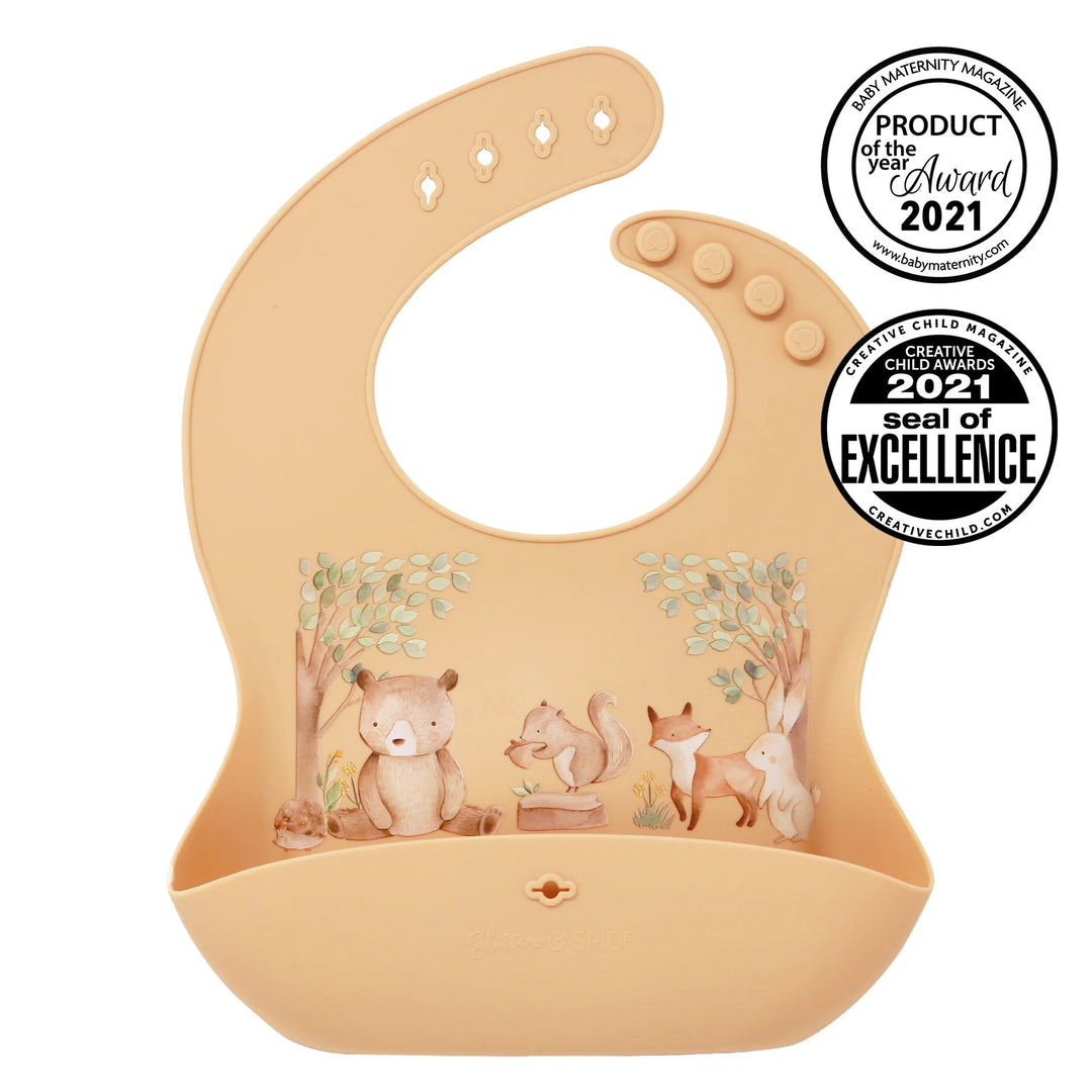 Beige silicone baby bib with woodland animal print, adjustable buttons, and award badges.