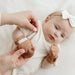 Cute baby lying on a bed with mommy putting on the Goumi anti scratch Mitts high prairie colour with hook and loop strap