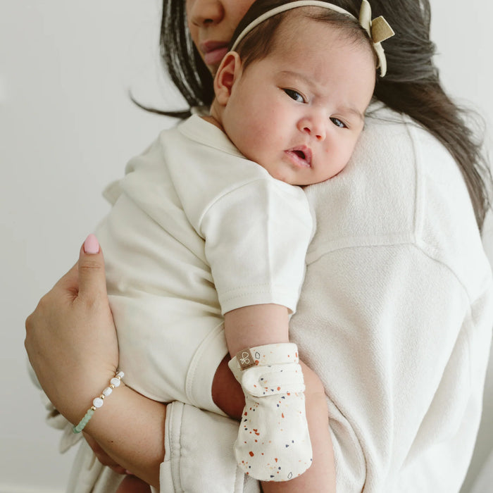 Baby in his mother's arms wearing the Goumi anti-scratch mitts Terrazzo - Goldtex