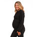 HERA black maternity top worn by a pregnant woman standing and smiling against a white background.