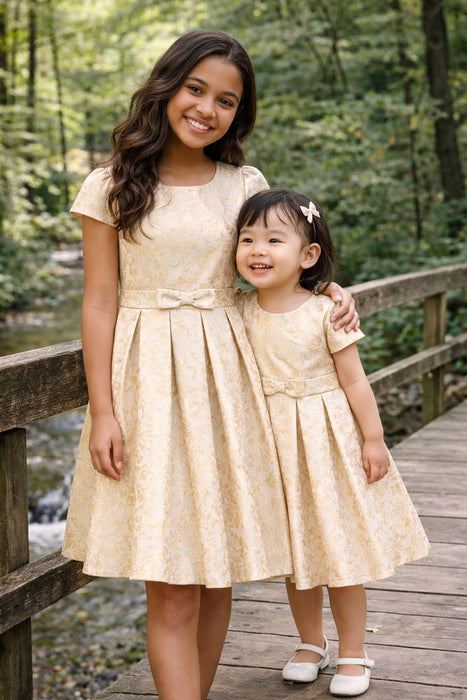 JKS81 yellow gold party dress worn by two girls standing together on a wooden bridge outdoors.
