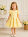 KIDS ENERGY Yellow Dress shown on smiling girl standing in a bright, floral-decorated room.