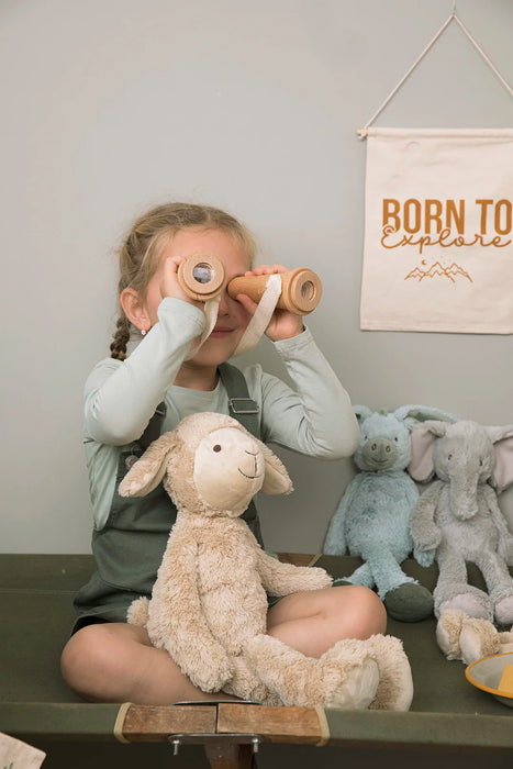 Child playing with wooden binoculars, holding plush sheep toy, nursery decor in background