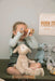Child playing with wooden binoculars, holding plush sheep toy, nursery decor in background