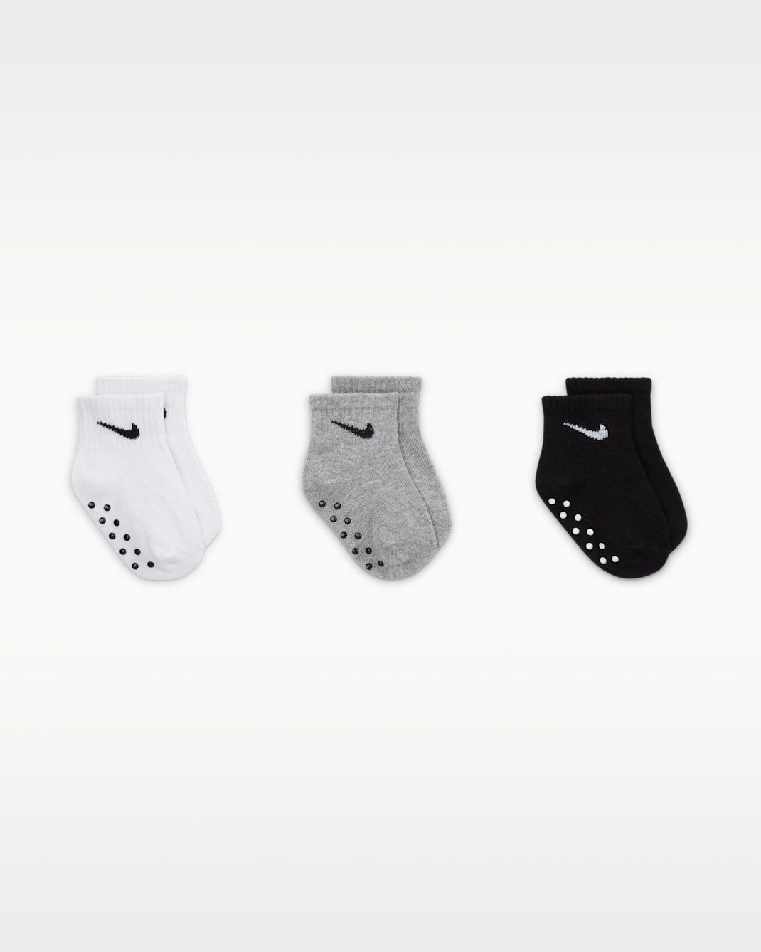Nike baby gripper socks in white, grey, and black shown in a row on a plain background.