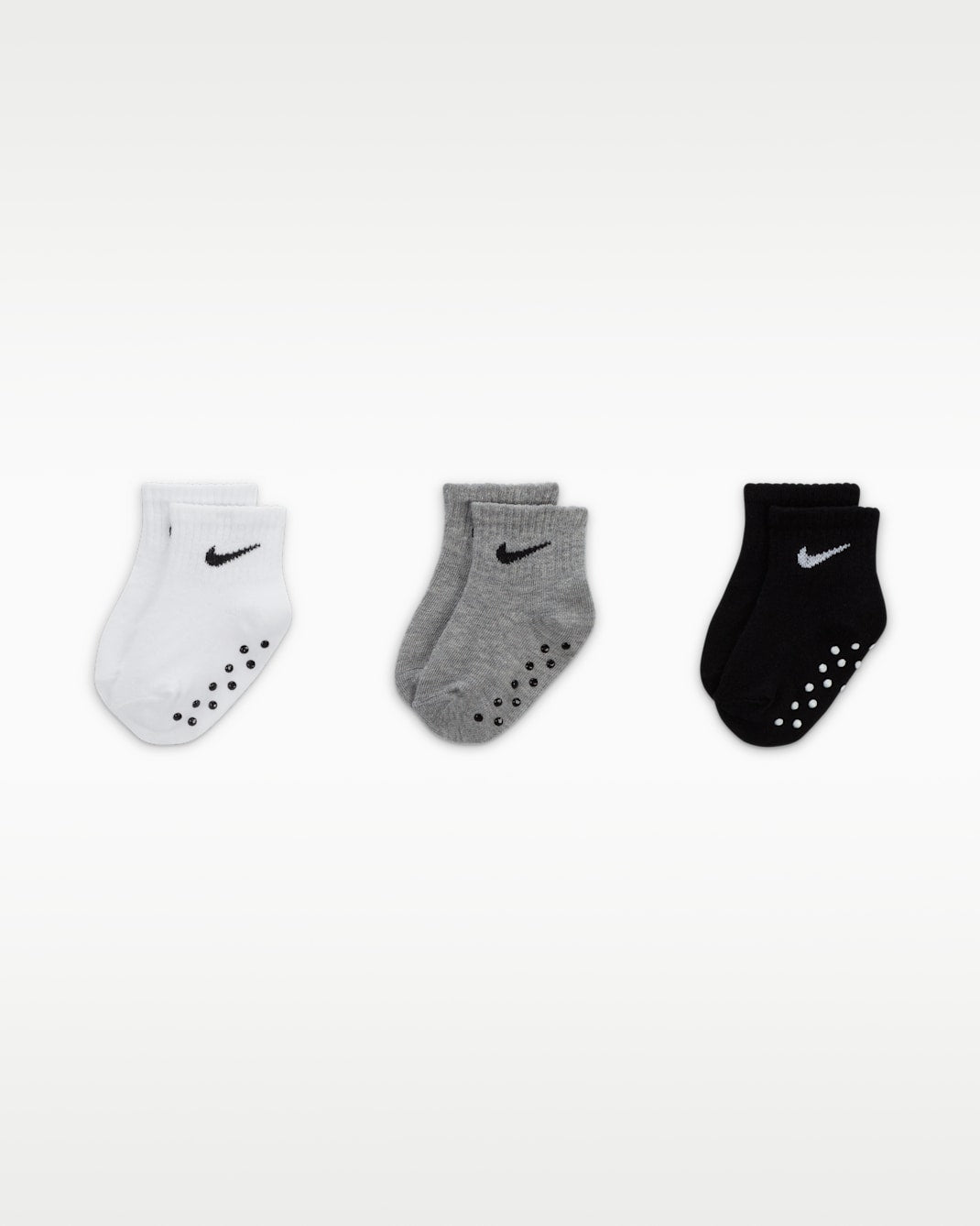 Nike baby gripper socks in white, grey, and black displayed side by side on a plain background.
