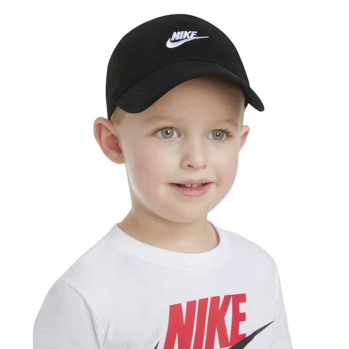 Nike kids’ black baseball cap worn by a child with a white Nike logo t-shirt on a white background.