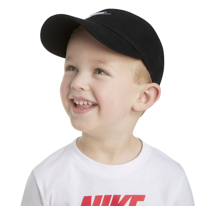Nike kids' black cap worn by a smiling child with a white logo t-shirt in a studio setting.